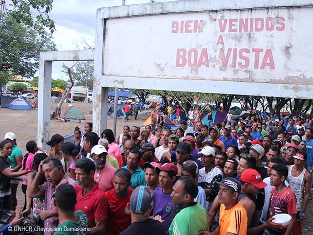 Multidão de imigrantes sob a placa de boas-vindas de Boa Vista