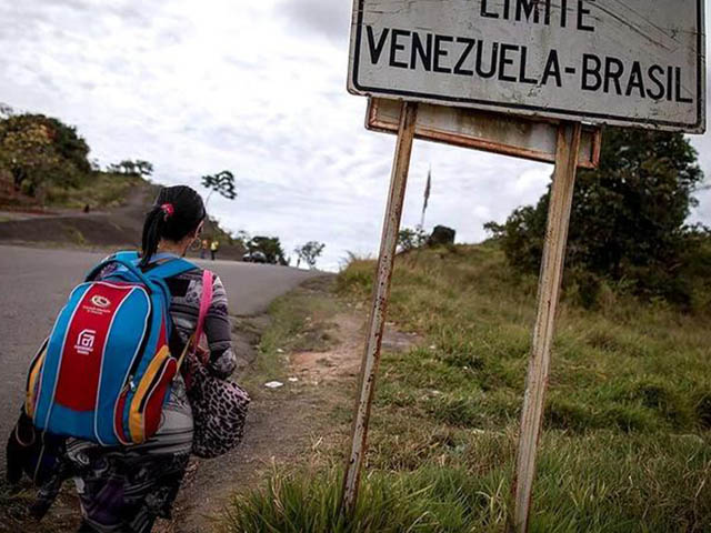 Imigrante caminhando junto à placa da fronteira Venezuela–Brasil